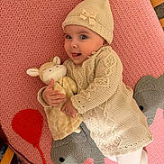 Dulce Maria is registered to the contest to win money with this photo: baby, infant, knit_hat, pom_pom, knit_sweater, plush_toy, giraffe, pink_blanket, crochet_elephant, crochet_balloon, cute, smiling, lying_down, soft_toy, child, indoor, cozy, warm_clothing, playful, young_child