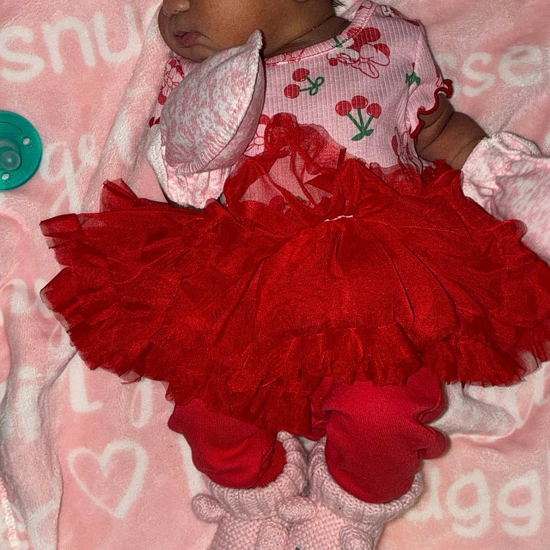 Loyalty is registered to the contest to win money with this photo: baby, sleeping, pink, red, tutu, headband, blanket, cute, infant, clothing, footwear, bunny_slippers, pattern, soft, cozy, resting, adorable, newborn, child, portrait