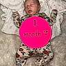 newborn, baby, sleeping, infant, portrait, floral_outfit, onesie, blanket, bed, pink_marker, one_month, text_overlay, face, closed_eyes, arms_outstretched, legs, indoor, cozy, photography, milestone