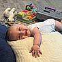 baby, pillow, smile, toy, stuffed_animal, floor, carpet, child, hand, onesie, indoor, playtime, happy, infant, reaching, crawling, colorful, soft_toy, head, expression