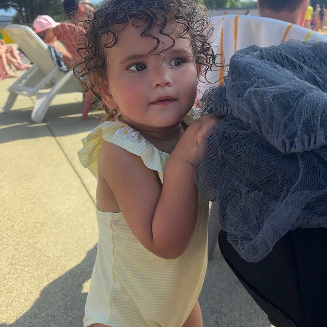 Sanah a rejoint le concours — aidez-le/la à gagner de superbes lots ! background, beach_chair, casual_clothing, child, curious, curly_hair, daylight, family, outdoor, park, people, person, recreation, stroller, summer, sunny, toddler, trees, vacation, yellow_romper