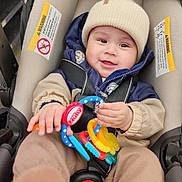 Thiago joined the competition — help win amazing prizes! baby, car_seat, toy, smile, hat, winter_clothing, jacket, pants, indoor, child, infant, happy, cute, playful, teething_toy, bundle_up, seatbelt, close_up, person, warm_clothes