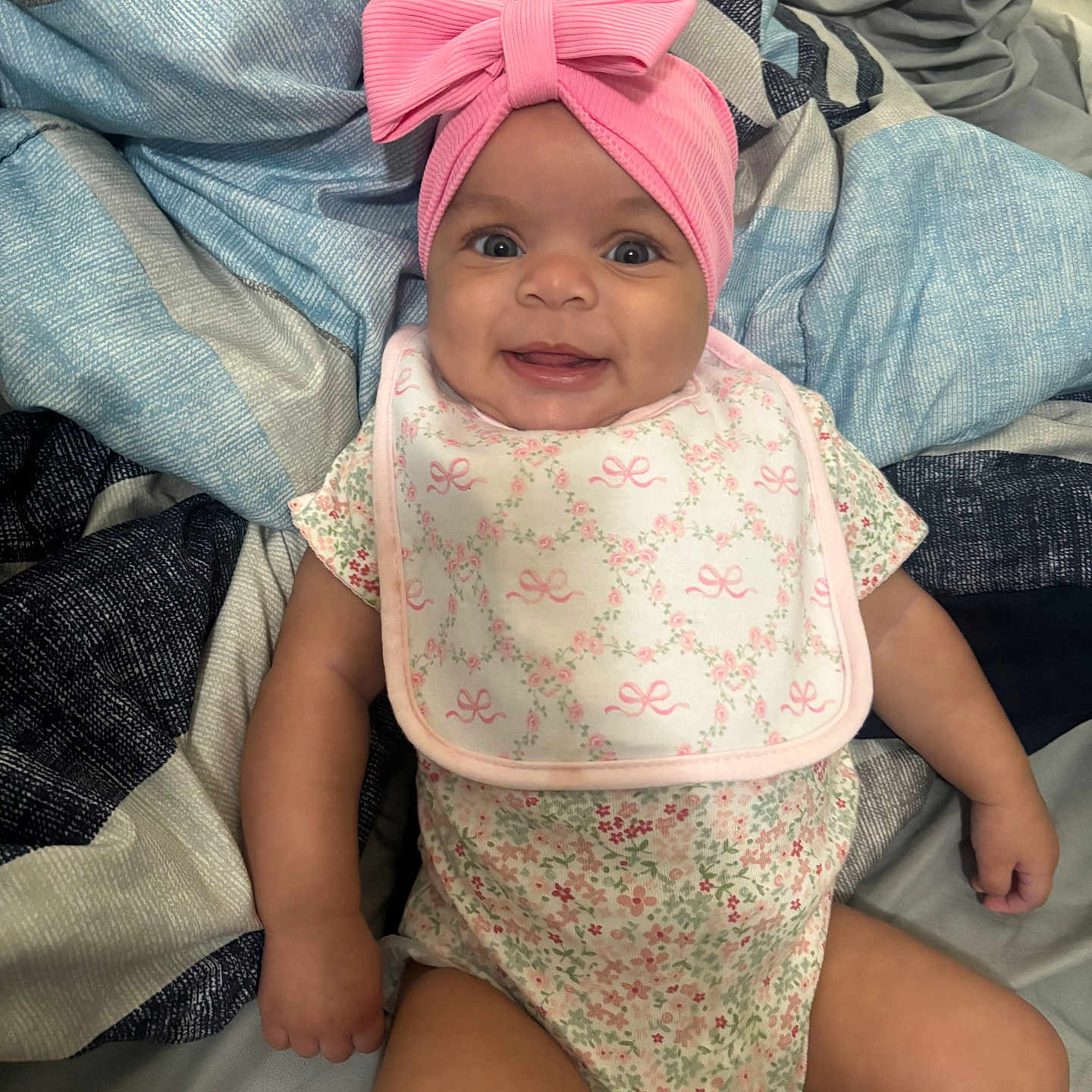 Romani joined the competition — help win amazing prizes! baby, bed, blanket, bow, child, clothing, cute, floral, happy, headband, infant, lying, onesie, person, pink, portrait, quilt, skin, smiling, young