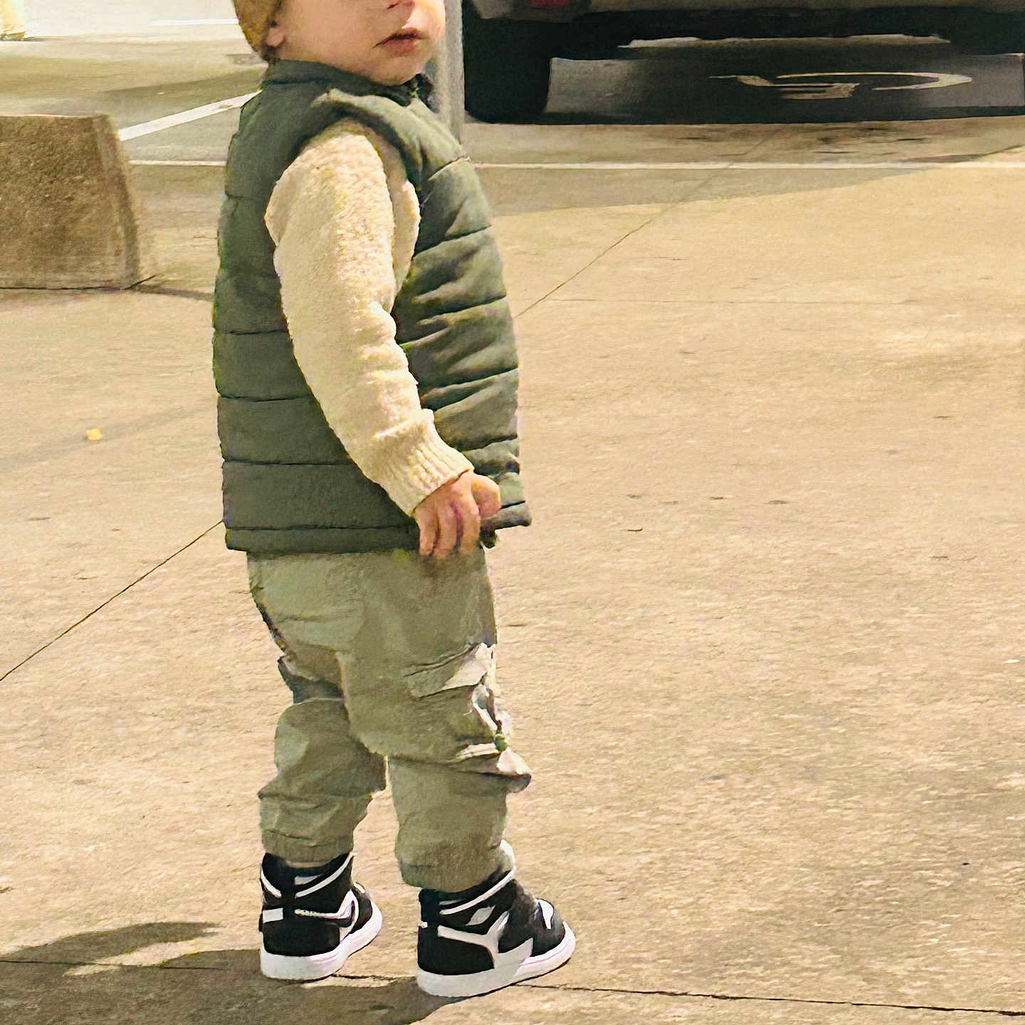 Miraç Mir a rejoint le concours — aidez-le/la à gagner de superbes lots ! beanie, car, cargo_pants, casual_clothing, child, concrete, daylight, fall_fashion, looking_back, outdoor, parking_lot, person, puffer_vest, shadow, side_view, sneakers, street_style, toddler, urban, young_child