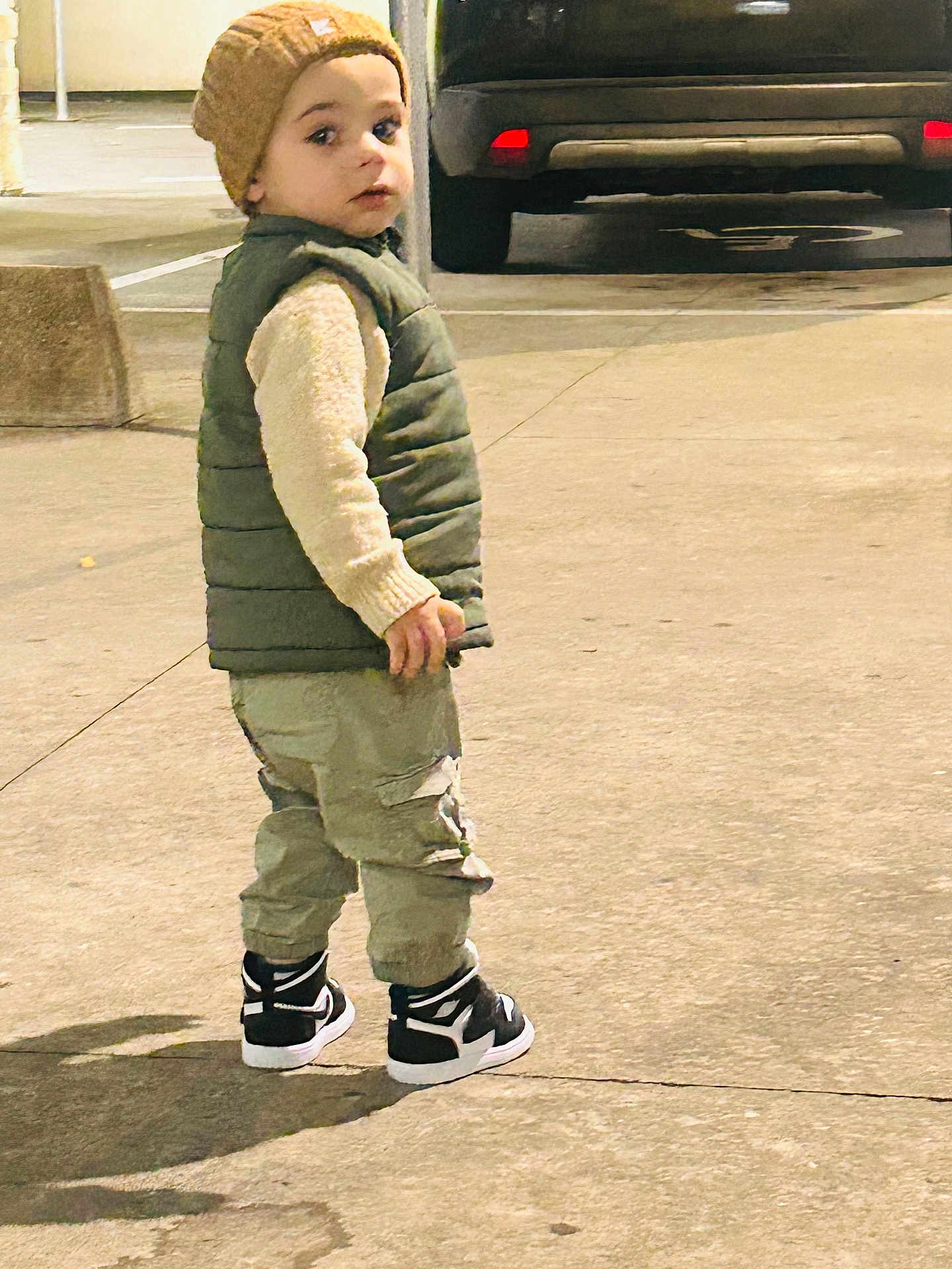 Miraç Mir a rejoint le concours — aidez-le/la à gagner de superbes lots ! toddler, child, beanie, puffer_vest, cargo_pants, sneakers, outdoor, side_view, shadow, concrete, parking_lot, car, casual_clothing, looking_back, street_style, young_child, fall_fashion, daylight, urban, person