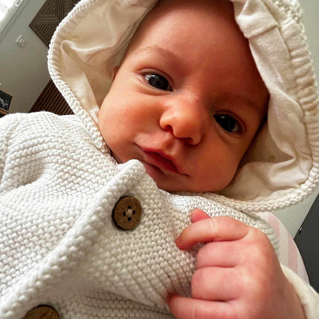 élio a rejoint le concours — aidez-le/la à gagner de superbes lots ! baby, infant, hoodie, knitted_clothing, white, cute, face, hand, indoor, portrait, cozy, child, newborn, button, warm, window, light, skin, candid, expression