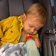 Joshua is registered to the contest to win money with this photo: baby, blanket, bottle, child, closed_eyes, corduroy, cozy, fabric, face, hair, indoors, infant, milk_bottle, nap, photography, portrait, seated, sleeping, stroller, yellow_jacket
