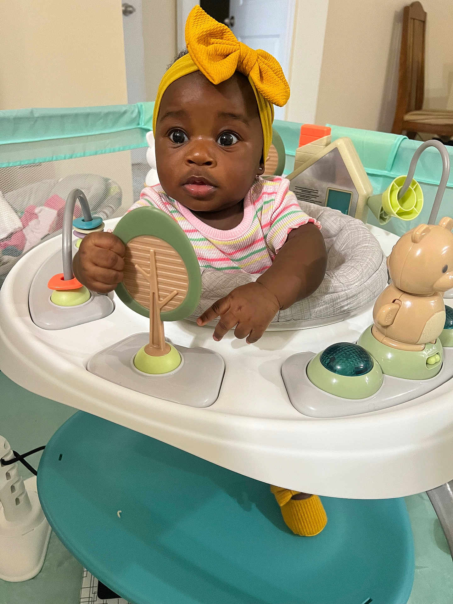 Joie joined the competition — help win amazing prizes! baby, child, indoor, toy, activity_center, yellow_bow, curious, playful, colorful, headband, infant, hands, face, eyes, clothing, footwear, furniture, plastic_toy, seat, person