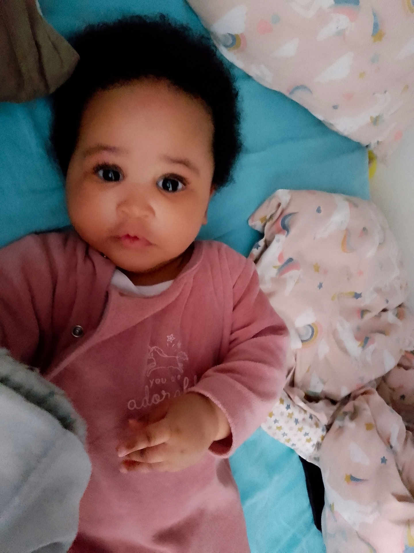 Keyana a rejoint le concours — aidez-le/la à gagner de superbes lots ! baby, infant, child, pink_clothing, blanket, unicorn_pattern, rainbow_pattern, bed, soft_toys, cute, lying_down, indoors, portrait, face, hand, curly_hair, expression, comfort, cozy, sleepwear