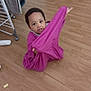 baby, child, clothing, curious, drying_rack, expression, face, floor, footwear, furniture, hand, home, indoor, person, playful, purple_cloth, room, sitting, toddler, wooden_floor