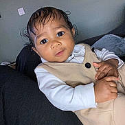 Tyler-Scott participe au concours pour gagner de l'argent avec cette photo : baby, child, indoor, person, face, curly_hair, clothing, beige_outfit, white_shirt, cute, resting, looking, young_child, portrait, skin, hand, sitting, cozy, dark_background, expression