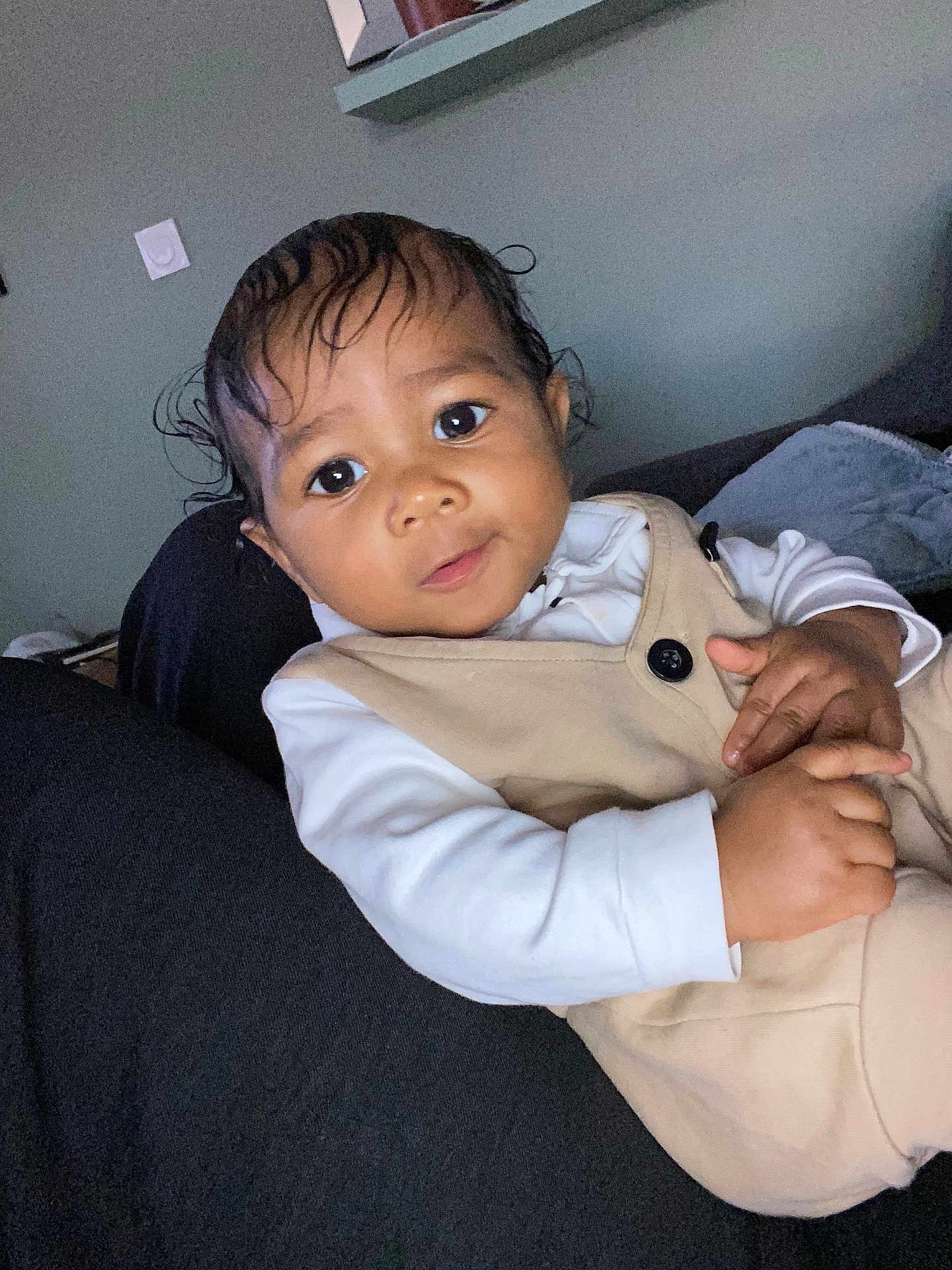 Tyler-Scott participe au concours pour gagner de l'argent avec cette photo : baby, child, indoor, person, face, curly_hair, clothing, beige_outfit, white_shirt, cute, resting, looking, young_child, portrait, skin, hand, sitting, cozy, dark_background, expression