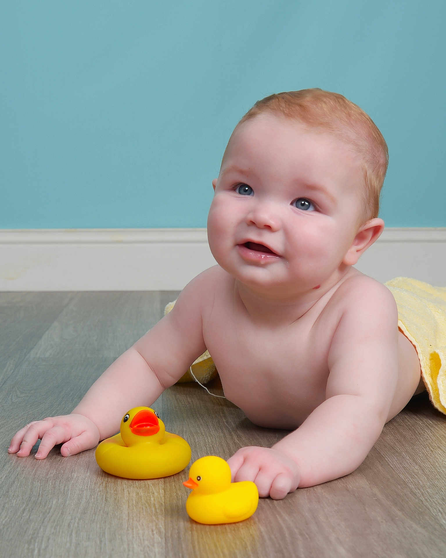 Luca joined the competition — help win amazing prizes! baby, child, rubber_duck, yellow_duck, floor, wooden_floor, towel, blue_wall, skin, face, hands, smile, indoor, cute, infant, play, toy, lying_down, childhood, happy