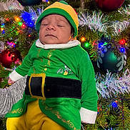 Patrick joined the competition — help win amazing prizes! baby, child, sleeping, christmas_tree, ornaments, holiday, festive, elf_costume, green_clothing, yellow_pants, red_ornaments, lights, pine_tree, seasonal, celebration, festivity, cute, holiday_decor, infant, costume