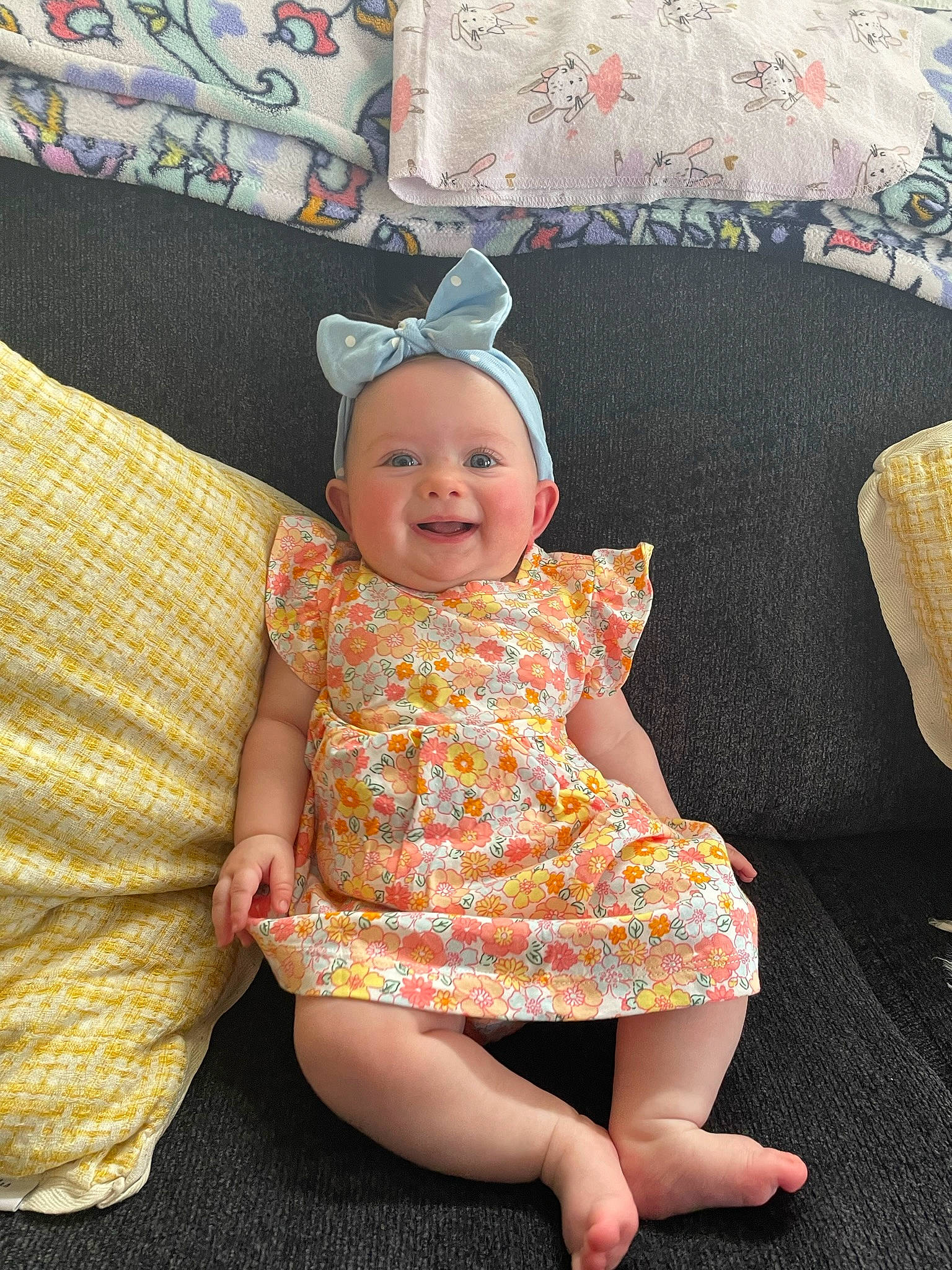 Ainsley is registered to the contest to win money with this photo: baby, baby_toddler_clothing, comfort, costume_hat, couch, day_dress, embellishment, face, happy, human_leg, joy, linens, one_piece_garment, pattern, person, pink, room, sleeve, smile, sun_hat