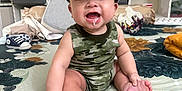 Drake joined the competition — help win amazing prizes! baby, child, smiling, drooling, cap, camo_clothing, sitting, bedspread, floral_pattern, foot, hand, indoor, sneaker, room, shelf, water_bottle, toy, fabric, person, happy