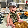 Drake joined the competition — help win amazing prizes! baby, child, cap, hat, camouflage_clothing, drool, sitting, bedspread, floral_pattern, footwear, sneaker, indoor, furniture, cubby_shelf, water_bottle, toy, curious, cute, infant, person