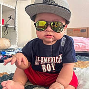 Drake joined the competition — help win amazing prizes! baby, child, sunglasses, cap, drool, sitting, indoor, bedspread, clothing, red_shorts, tshirt, reflection, face, foot, hand, person, cute, casual, expression, home
