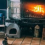 animal, cat, cat_sitting, cozy, decor, domestic, fire, fireplace, furniture, hearth, home, indoor, living_room, pet_house, relaxation, sitting, stone_wall, tiled_floor, warm_light, warmth
