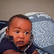 Legend joined the competition — help win amazing prizes! baby, infant, child, portrait, face, eyes, wide_eyed, indoor, bedroom, blanket, bedding, fish_pattern, clothing, dark_shirt, sitting, looking_at_camera, television, home, closeup, photography
