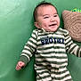 baby, smiling, infant, striped_clothing, onesie, green_mat, pillow, toy, happy, dimples, lying_down, child, cute, indoor, playtime, young_child, person, face, apparel, fabric