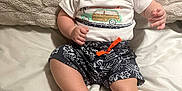 Brian is registered to the contest to win money with this photo: baby, bed, casual, child, chubby_cheeks, clothing, cute, footwear, happy, indoors, infant, person, pillow, portrait, sandals, shorts, sitting, smiling, white_tshirt, young_child