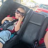 child, toddler, car_seat, sunglasses, car_interior, seatbelt, smiling, red_shirt, shorts, road, car, traffic, window, daylight, seat, leather, safety, cute, baby, travel