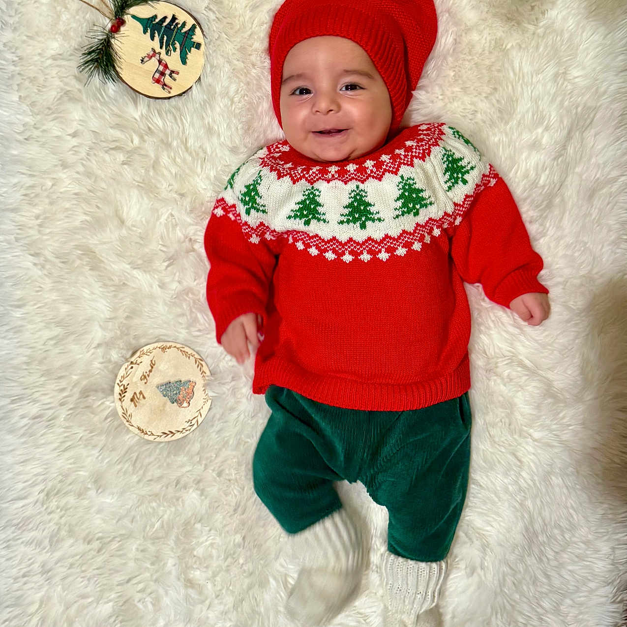 Nicolas is registered to the contest to win money with this photo: baby, child, christmas, christmas_sweater, cute, festive, fluffy_rug, green_pants, holiday, holiday_decor, indoor, ornament, person, portrait, red_hat, red_sweater, smile, smiling, white_socks, wooden_decoration