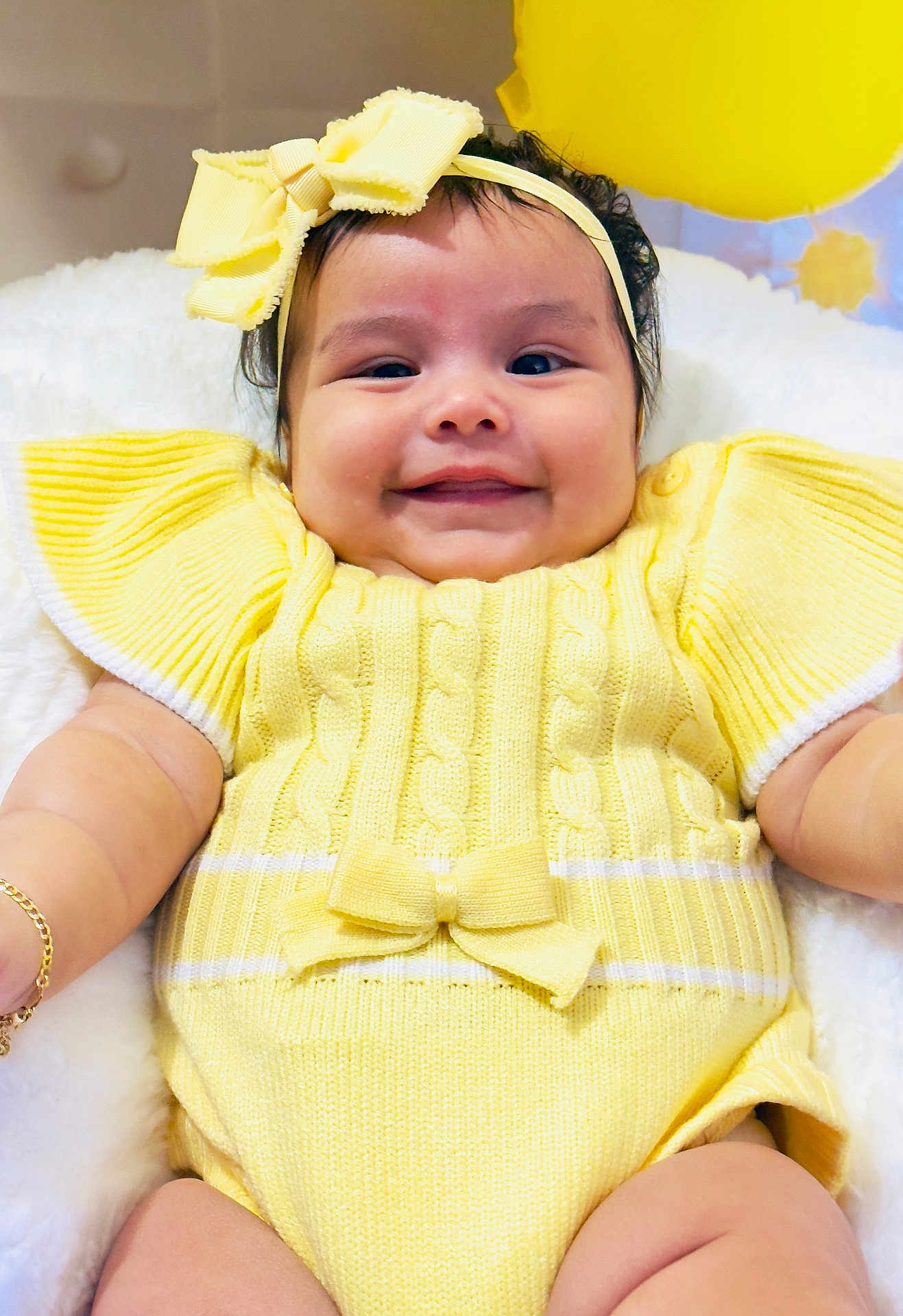 Helena joined the competition — help win amazing prizes! baby, smile, yellow_clothing, headband, bow, infant, knitwear, cheeks, happy, cute, arm, bracelet, balloon, soft_background, portrait, child, indoors, closeup, person, cuteness