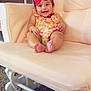 baby, child, smiling, pink_bow, floral_clothing, rocking_chair, beige_chair, indoor, carpet, baby_accessories, organizer, books, happy, cute, infant, portrait, sitting, comfortable, room, headband