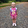 child, girl, smiling, backpack, pink_shirt, shorts, sneakers, outdoor, gravel_path, trees, nature, daylight, happy, standing, casual_clothing, forest, young, person, portrait, summer