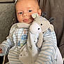 baby, infant, plush_toy, giraffe, blue_eyes, striped_pajamas, smile, face, child, seated, soft_toy, cute, indoor, cozy, blanket, cushion, comfort, portrait, young_child, happy