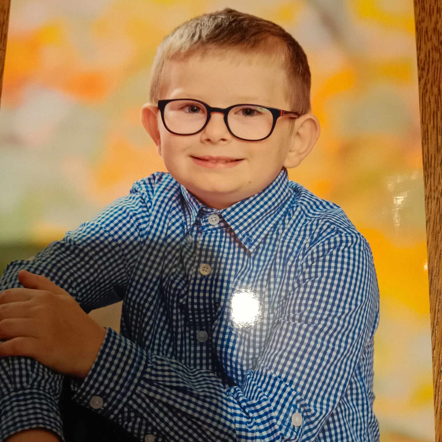Lenny participe au concours pour gagner de l'argent avec cette photo : child, boy, glasses, blue_shirt, checkered, portrait, smile, face, short_hair, sitting, indoor, background_blur, wooden_surface, casual, young, person, photography, happy, eyewear, clothing