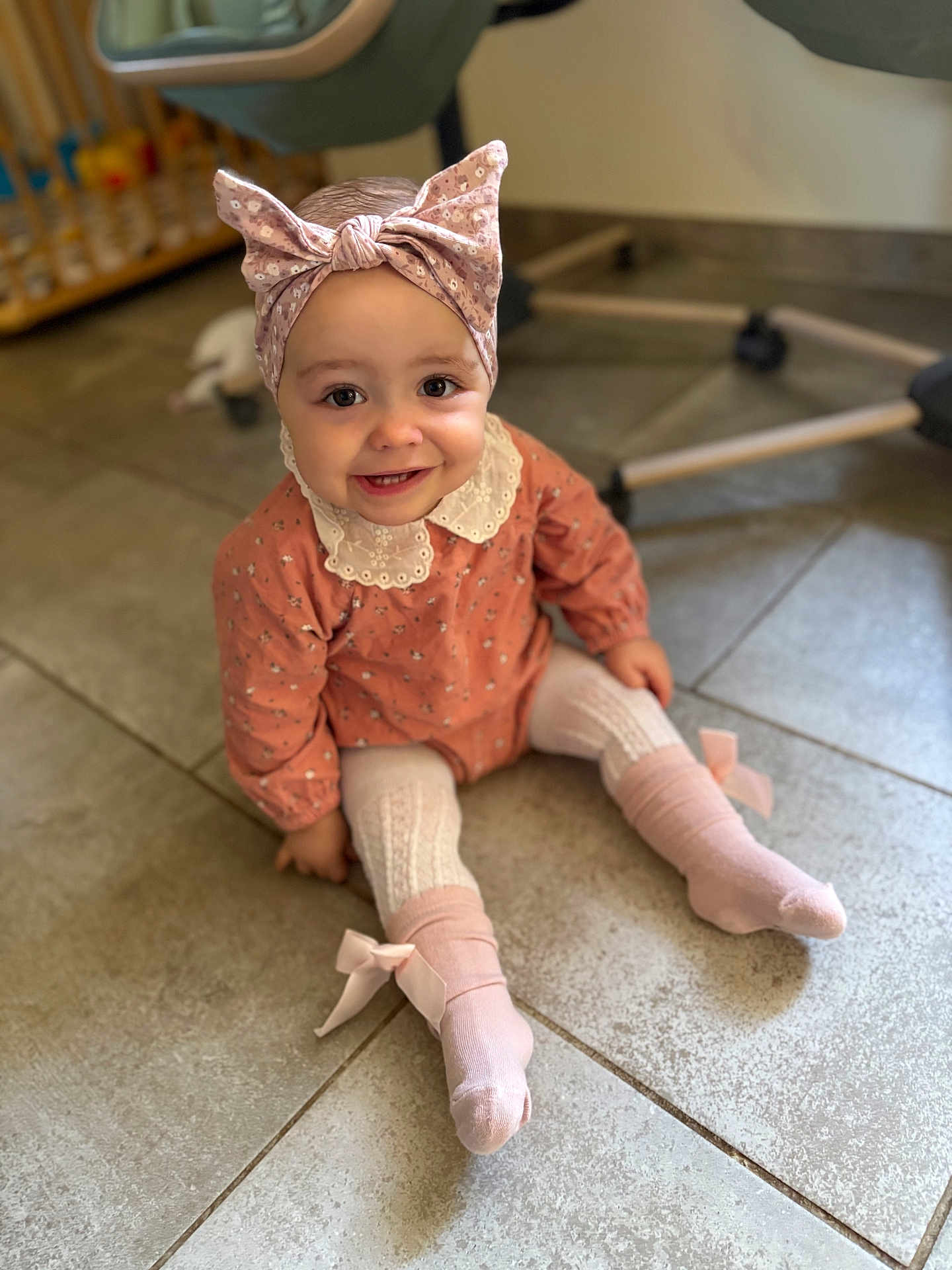 Hanaé a rejoint le concours — aidez-le/la à gagner de superbes lots ! toddler, child, smiling, bow_headband, pink_socks, lace_collar, sitting, floor, tiles, indoor, cute, happy, clothing, portrait, baby, headwear, feet, playroom, person, young_child