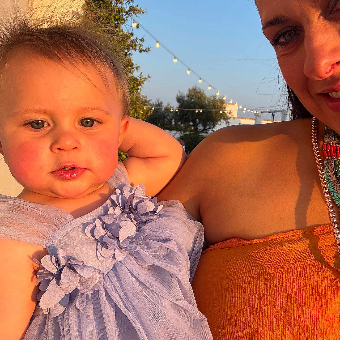 Bea is registered to the contest to win money with this photo: blue_sky, child, dress, event, face, fashion, happy, holding, lavender, nature, orange, outdoor, person, portrait, smile, string_lights, sunlight, toddler, trees, woman