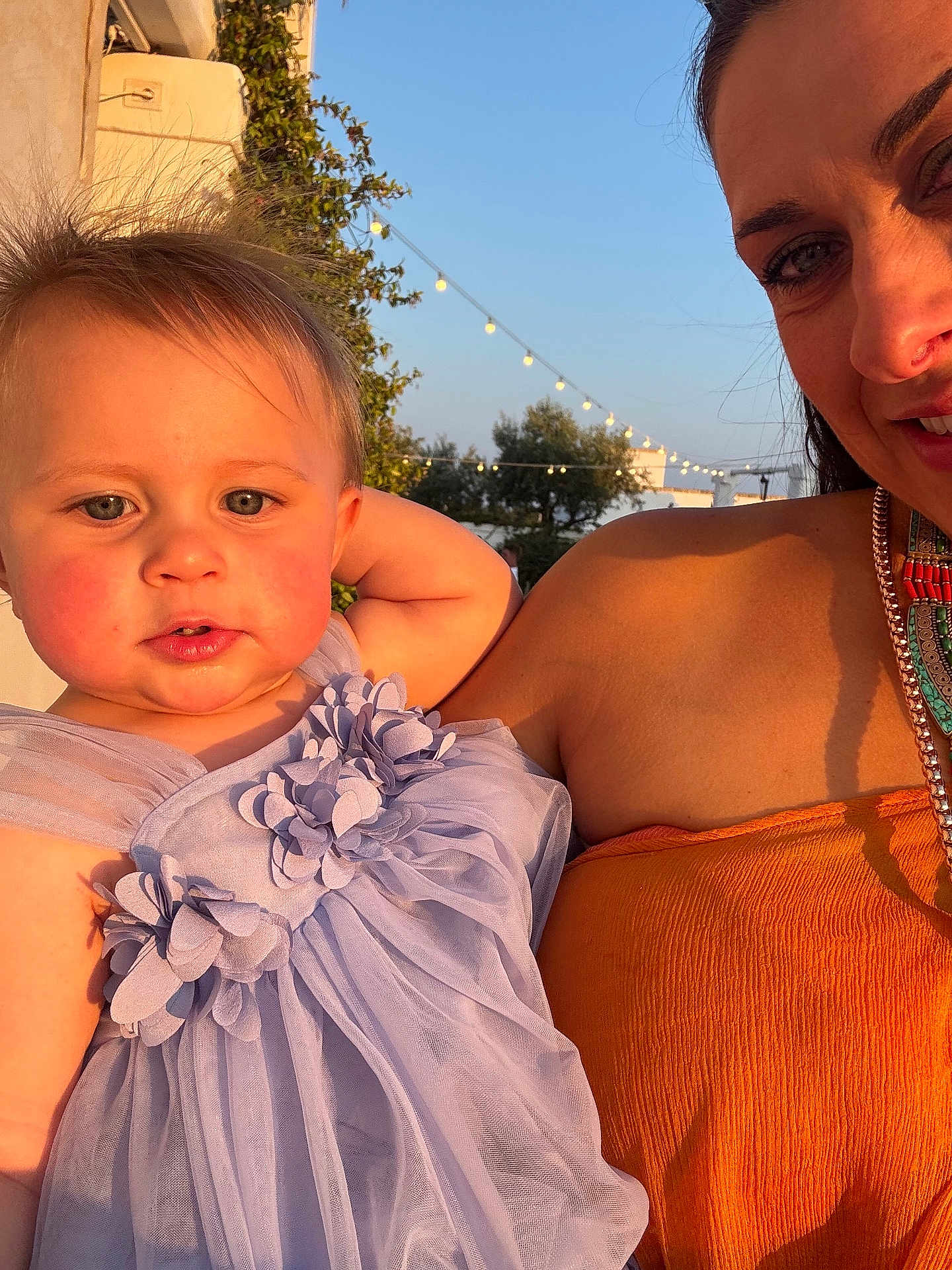 Bea is registered to the contest to win money with this photo: toddler, child, woman, outdoor, dress, lavender, orange, smile, face, portrait, string_lights, sunlight, blue_sky, trees, holding, happy, fashion, person, nature, event