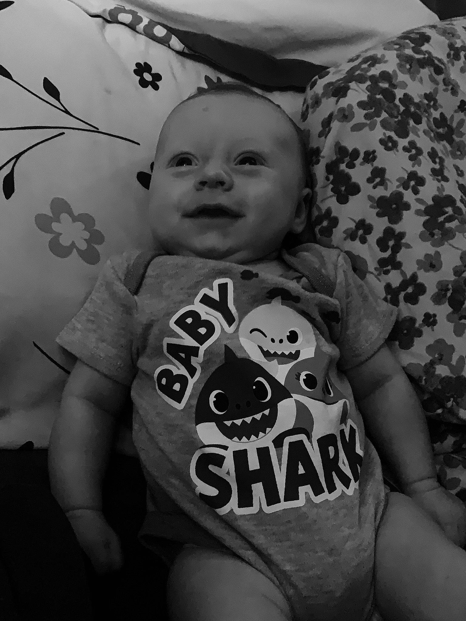 Kian is registered to the contest to win money with this photo: baby_toddler_clothing, black_and_white, cheek, facial_expression, finger, grey, happy, head, human, iris, mammal, organ, person, skin, sleeve, smile, standing, style, textile, vertebrate