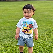 Elijah joined the competition — help win amazing prizes! toddler, child, grass, outdoor, shorts, tshirt, curly_hair, standing, greenery, playful, daylight, nature, young_child, casual_clothing, person, cute, summer, feet, expression, park