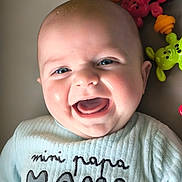 Evann a rejoint le concours — aidez-le/la à gagner de superbes lots ! baby, smile, blue_eyes, infant, clothing, text_on_clothing, toy, colorful, happy, face, portrait, cute, child, indoors, closeup, person, sitting, playful, expression, skin