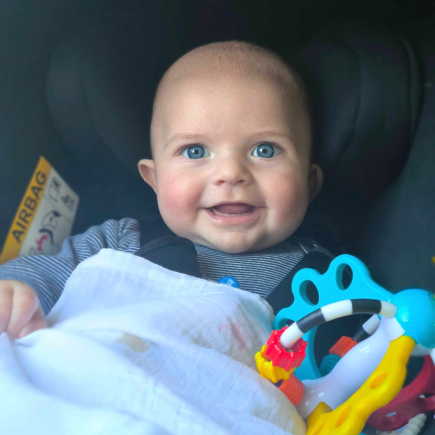 Evann participe au concours pour gagner de l'argent avec cette photo : baby, blue_eyes, smile, blanket, car_seat, toy, colorful, infant, happy, child, face, person, cute, clothing, striped_shirt, indoors, closeup, head, cheeks, seatbelt