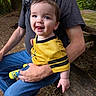 baby, child, person, adult, outdoor, forest, bench, yellow_jersey, smile, tongue_out, happy, blue_jeans, hand, nature, casual_clothing, wood, greenery, daylight, sitting, portrait