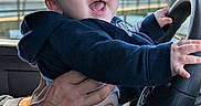 Paxxton is registered to the contest to win money with this photo: baby, child, infant, person, hand, steering_wheel, car_interior, clothing, hoodie, smile, happy, blue_eyes, window, outdoor, water, railing, daylight, portrait, holding, playful