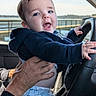 baby, child, infant, person, hand, steering_wheel, car_interior, clothing, hoodie, smile, happy, blue_eyes, window, outdoor, water, railing, daylight, portrait, holding, playful