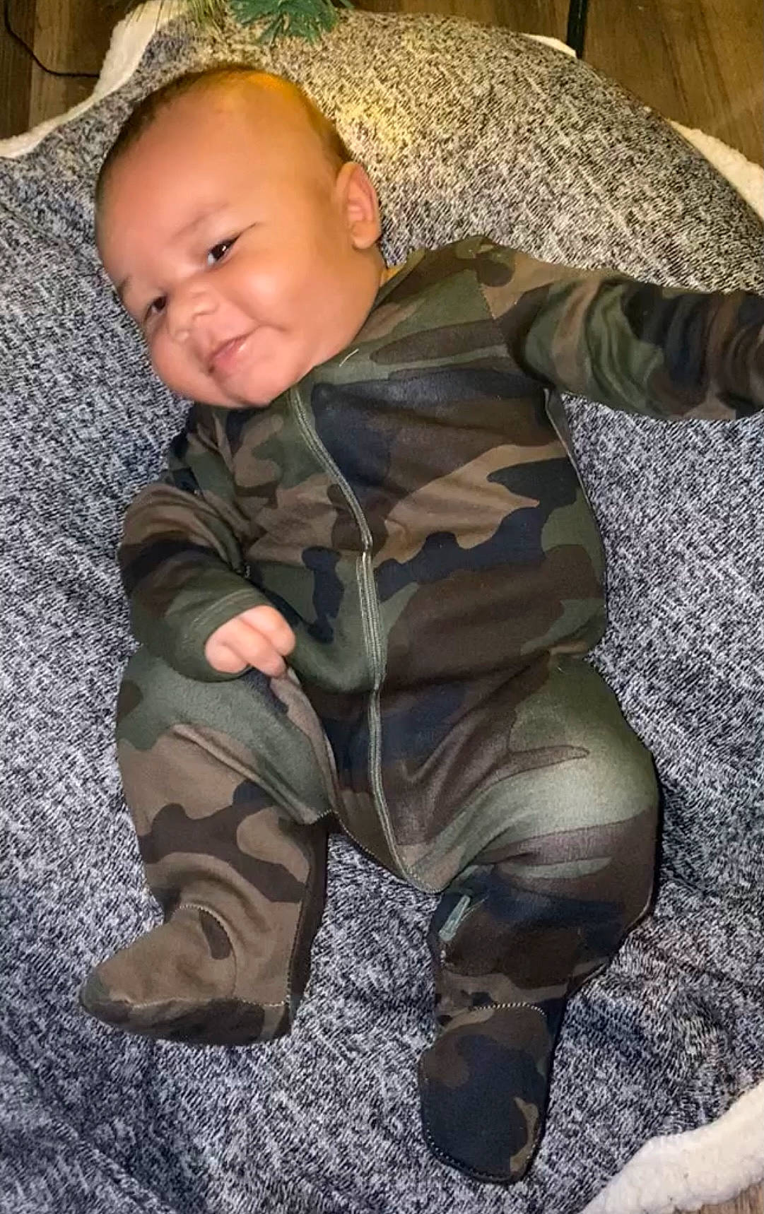 Carter is registered to the contest to win money with this photo: baby, baby_toddler_clothing, brown, camouflage, child, comfort, face, flooring, fur, grass, head, military_camouflage, military_uniform, pattern, person, sitting, skin, sleeve, smile, toddler