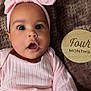 baby, infant, child, pink_clothing, headband, surprised_expression, face, eyes, mouth_open, blanket, wooden_sign, four_months, lying_down, indoors, cute, portrait, soft_texture, young, skin, person