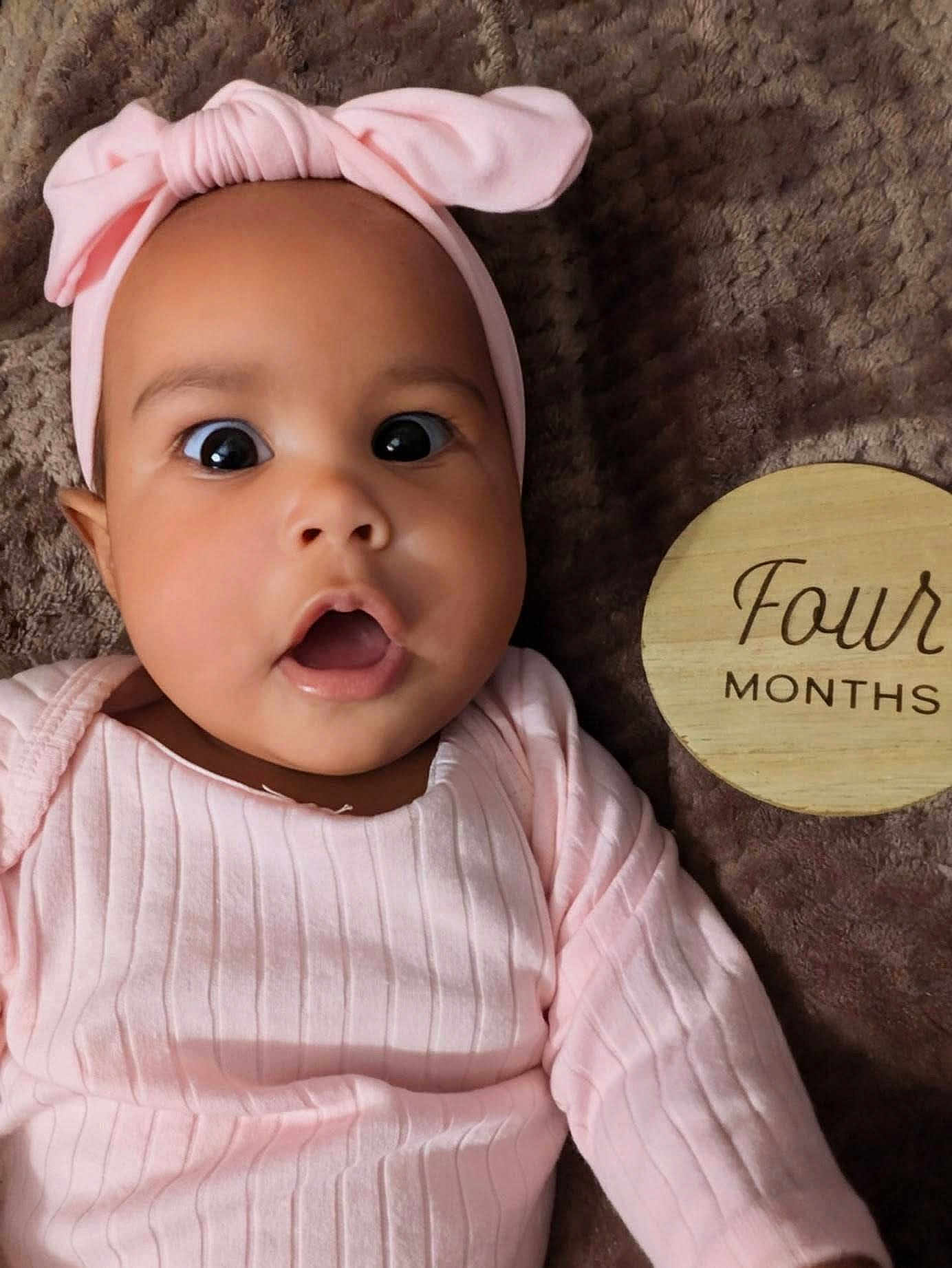 Carlarae joined the competition — help win amazing prizes! baby, infant, child, pink_clothing, headband, surprised_expression, face, eyes, mouth_open, blanket, wooden_sign, four_months, lying_down, indoors, cute, portrait, soft_texture, young, skin, person