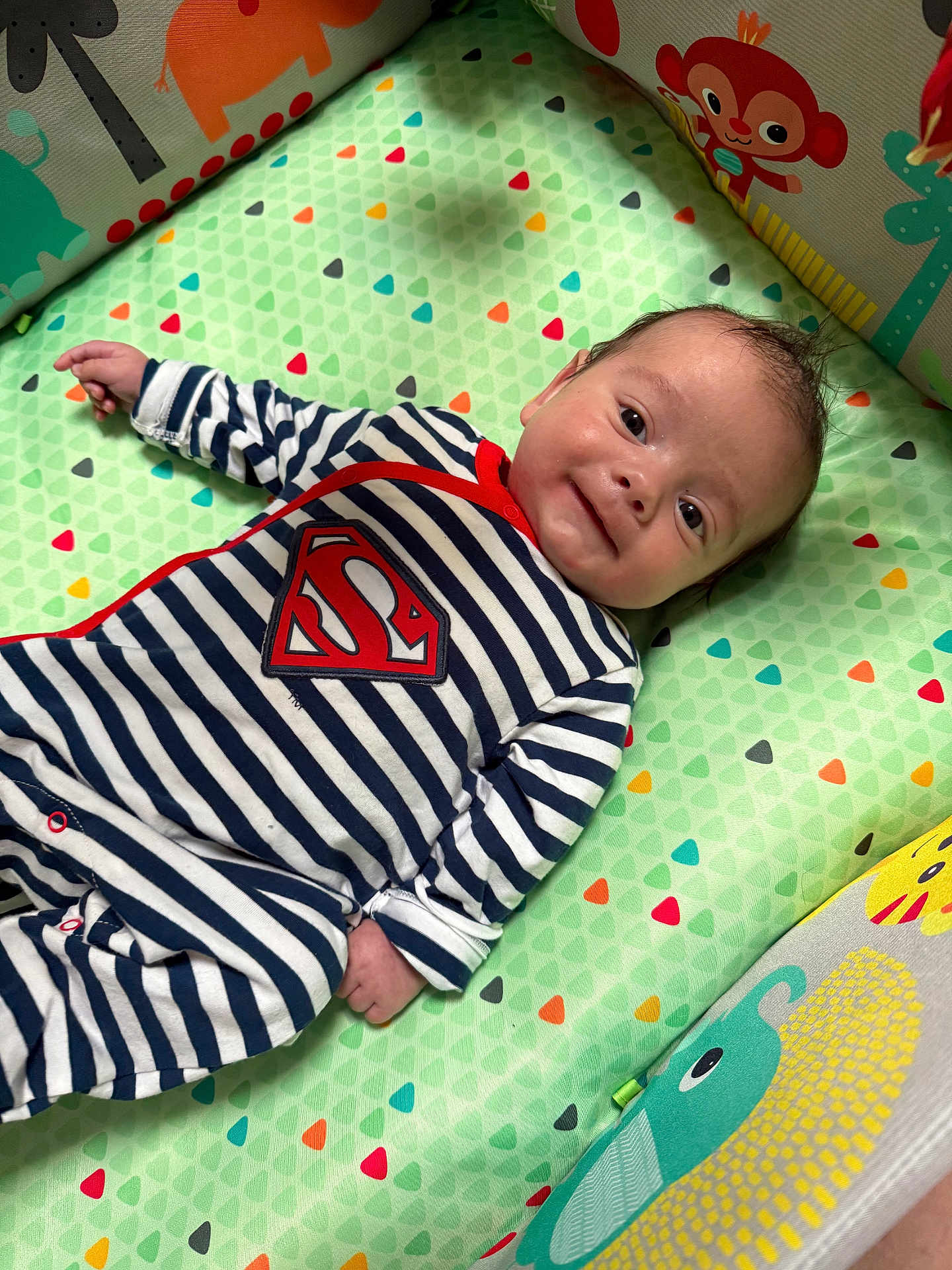 Rafael participe au concours pour gagner de l'argent avec cette photo : baby, infant, striped_clothing, superman_logo, play_mat, animal_prints, smile, lying_down, cute, child, indoors, colorful, soft_toys, happy, face, person, young_child, striped_onesie, cushion, play_area