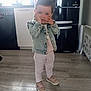 Anna a rejoint le concours — aidez-le/la à gagner de superbes lots ! toddler, child, denim_jacket, pink_shoes, light_pants, kitchen, refrigerator, flooring, cabinet, window, indoor, person, hands_on_face, playful, casual_clothing, young_child, home_interior, wood_floor, appliance, daylight