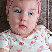 Venus is registered to the contest to win money with this photo: baby, child, face, blue_eyes, headband, flower, pink, white_clothing, floral_pattern, cute, portrait, chubby_cheeks, sitting, indoors, soft_light, skin, earrings, young_child, infant, comfortable