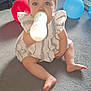 baby, child, bottle, milk, blue_eyes, dress, carpet, balloons, indoor, sitting, cute, person, infant, milk_bottle, floor, play_area, happy, light, home, young_child